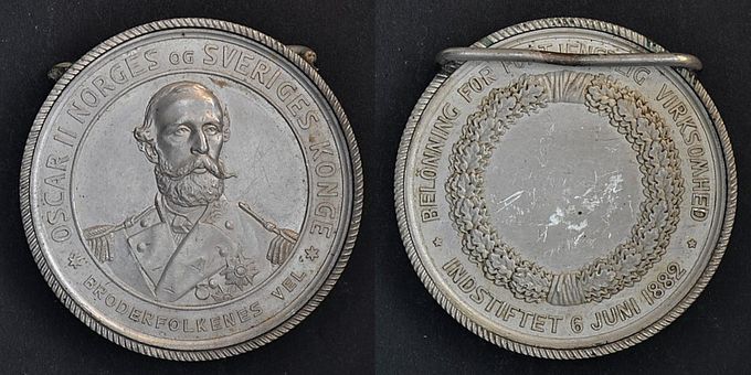 Kong Oscar IIs Bekönning for Fortjenstlig Virksomhed (Fortjenstmedaljen), innstiftet 6. juni 1882.  Gravert av Wilhelm Kullrich og preget ved Berliner Medaillen-Münze. Referanse Kvist nr. 81, type II. 25 gullmedaljer og 78 sølvmedaljer ble utdelt av denne typen.  Dette er et meget sjeldent avslag i aluminium. Medaljen er 31 mm og ligger løst i en ramme av aluminium med en påloddet festanordning. Bildet viser medaljen med og uten ramme. Toppstykken, en krone med ornament, er fjernet fra rammen ser det ut til. Hva denne aluminiumsutgaven er brukt til er usikkert, men den kan ha blitt laget for utstillinngsformål. Uansett en meget sjelden medalje med et flott portrett av kong Oscar II.